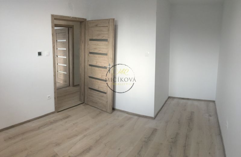 Szoba egy háromszobás lakásban, fa dekoros padlóval és világos falakkal.