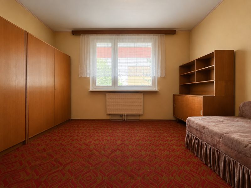 Nappali egy kétszobás lakásban, piros szőnyeggel, régi bútorokkal és ablakkal.