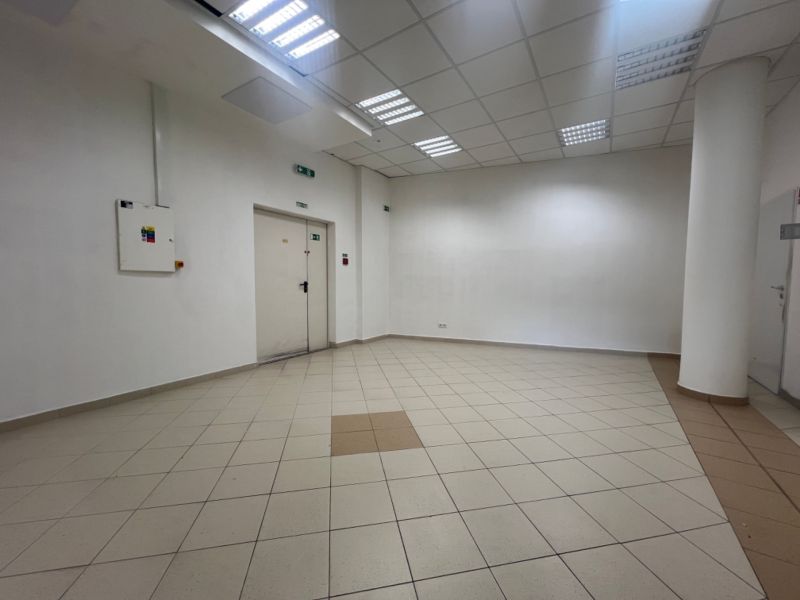 Üres üzlethelyiség csempézett padlóval, fehér falakkal, mennyezeti világítással.