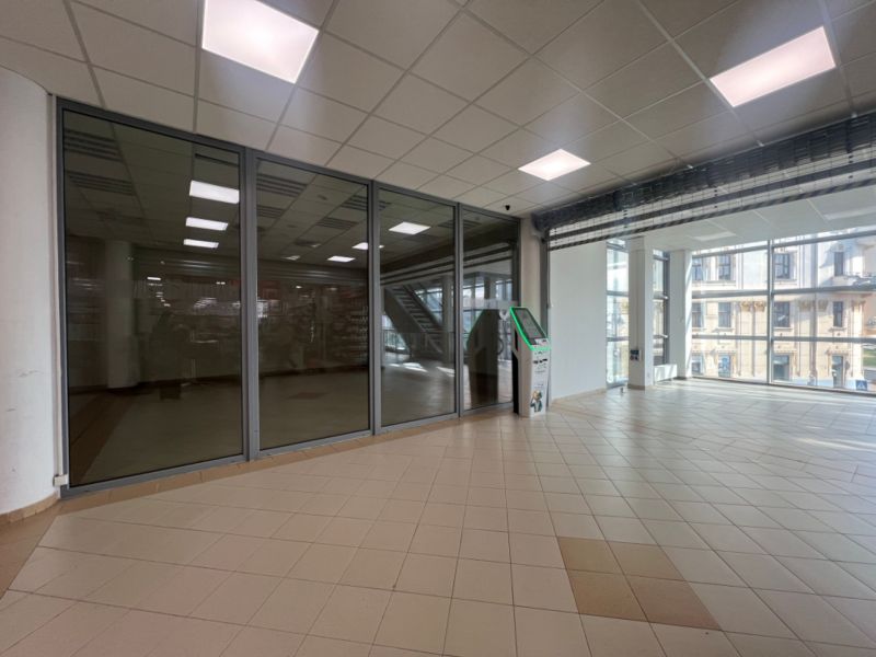 Üvegfalú üzlethelyiségek csempével és bankautomatával, belső tér nagy ablakokkal.