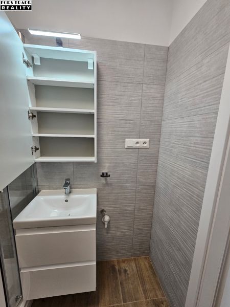 Fürdőszoba a garzonlakásban mosdóval és fa mintázatú padlóval.