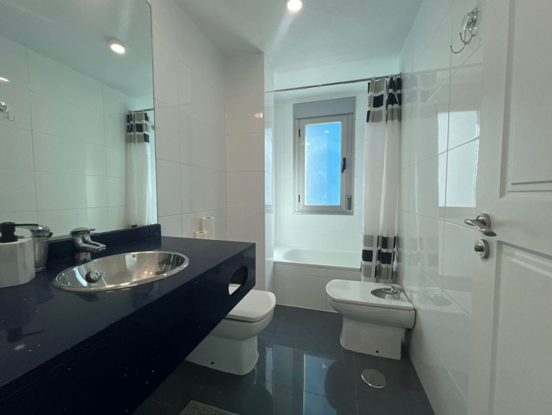 Fürdőszoba üdülő apartmanban káddal és mosdóval sötét pulton.
