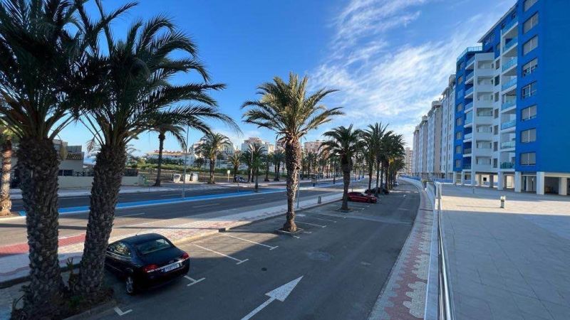 Pálmafák és az út mentén parkoló autók apartmanok mellett La Manga del Mar Menorban, Spanyolország.