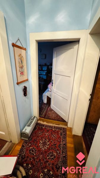 Szoba egy háromszobás lakásban szőnyeggel és nyitott ajtókkal, fa dekoros padlóval.