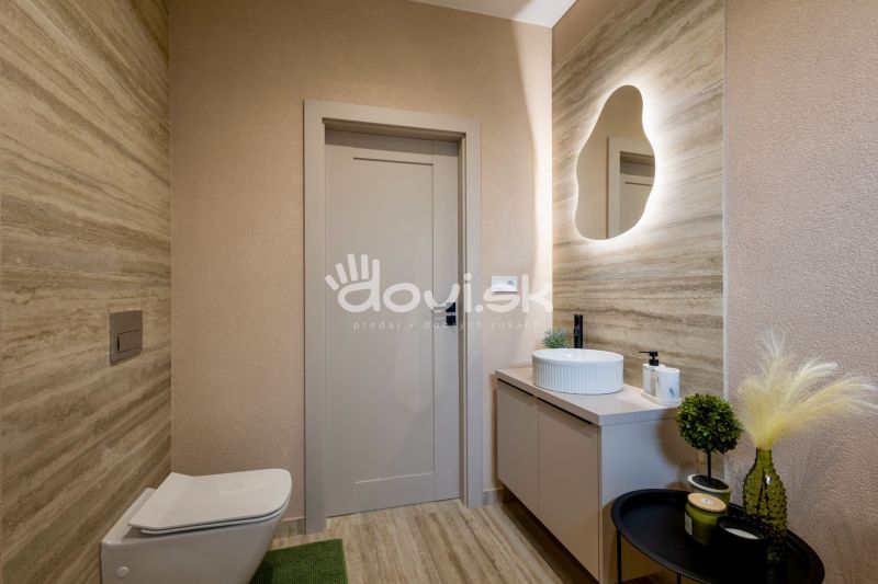 Családi ház fürdőszobája mosdóval és LED tükörrel, dekoratív növényekkel.