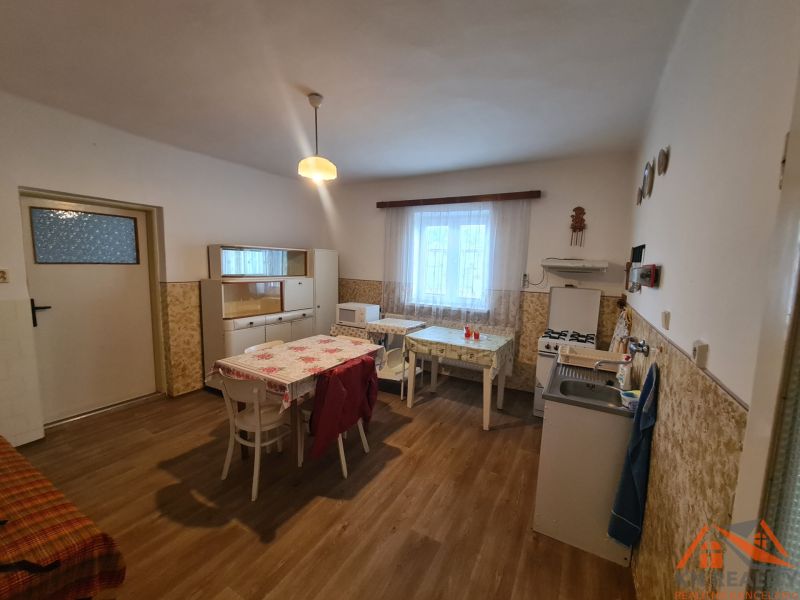 Konyha egy családi házban, fa dekoros padlóval, egyszerű bútorokkal és étkezőasztallal.