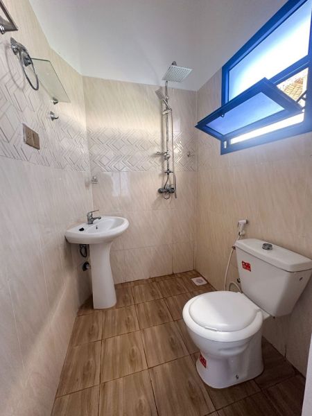 Fürdőszoba mosdóval, zuhanyzóval és WC-vel egy családi házban, fa mintázatú padlóval.