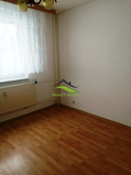 Szoba egy háromszobás lakásban fa dekoros padlóval, függönnyel és radiátorral.