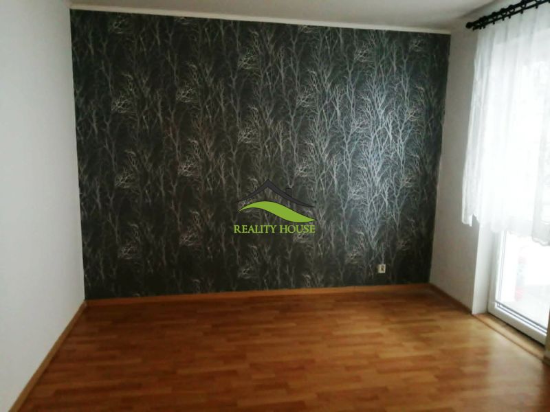 Szoba egy háromszobás lakásban fa dekor padlóval és mintás tapétával.
