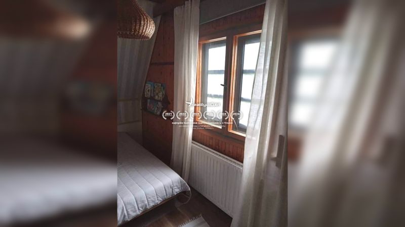 Szoba egy családi házban sötét fa burkolattal és ággyal az ablak mellett.