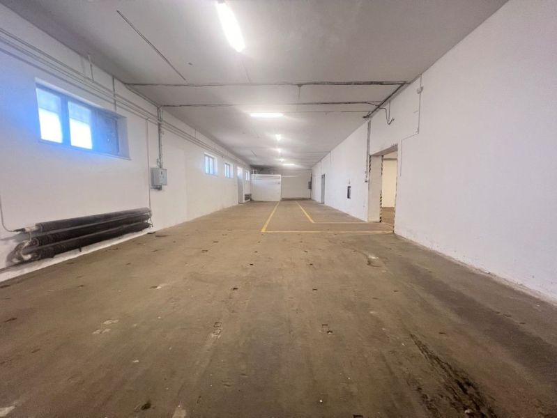 Raktár belső betonpadlóval és fehér falakkal, fénycsöves világítással.