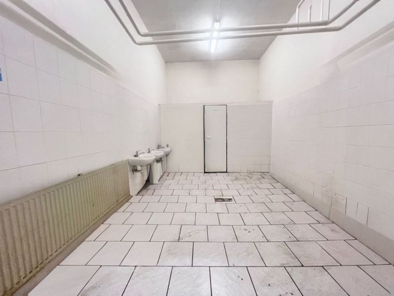 Raktárak és csarnokok belső tere fehér falakkal, két mosdóval és csempézett padlóval.