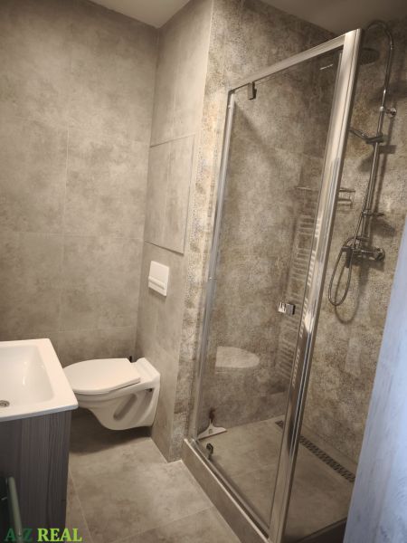 Fürdőszoba egy kétszobás lakásban, walk-in zuhanyzóval és WC-vel, minden szürke színvilágban.