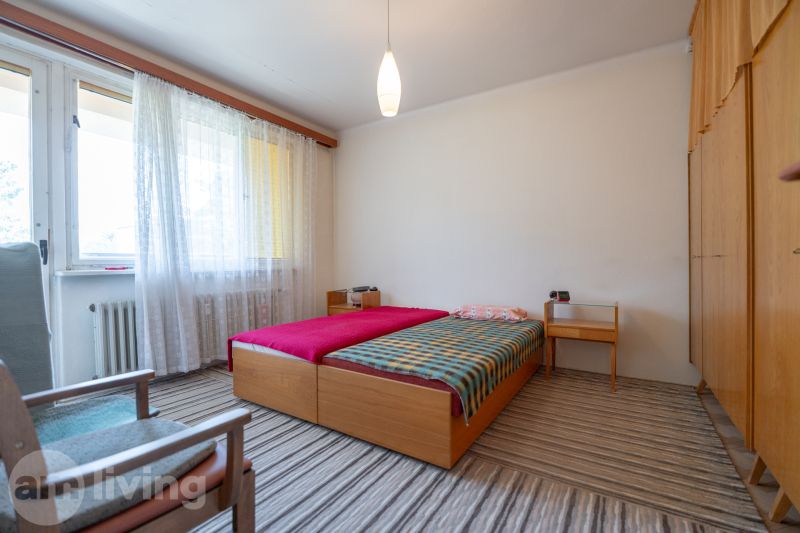 Hálószoba világos szőnyeggel és ággyal egy háromszobás lakásban.