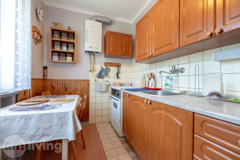 Konyha egy háromszobás lakásban fa szekrényekkel és étkezőasztallal.