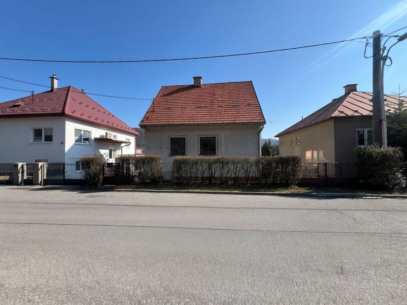Családi ház Besztercebányán piros tetővel és bokor kerítéssel.