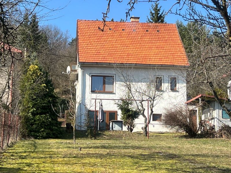 Családi ház Kráľovában, Besztercebányán, piros tetővel, zölddel és fákkal körülvéve.