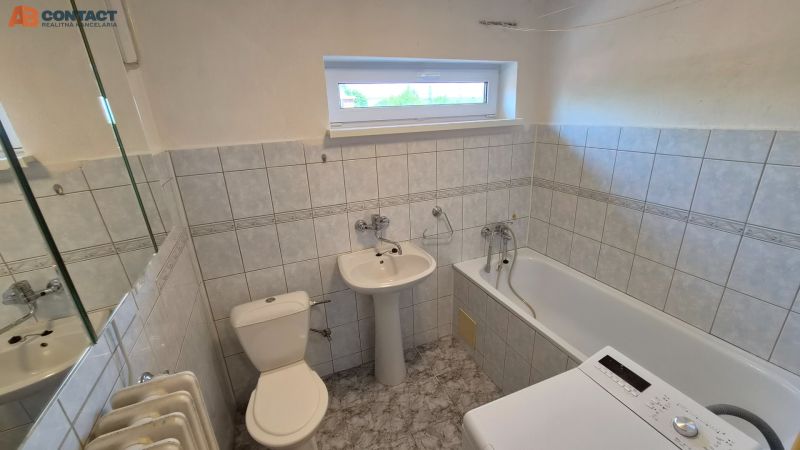 Fürdőszoba egy kétszobás lakásban káddal, mosdóval, mosógéppel és csempézett falakkal.