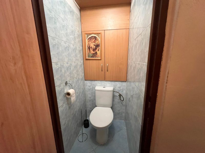 Kétszobás lakás WC-je kék csempékkel és fa dekorációjú szekrényekkel.