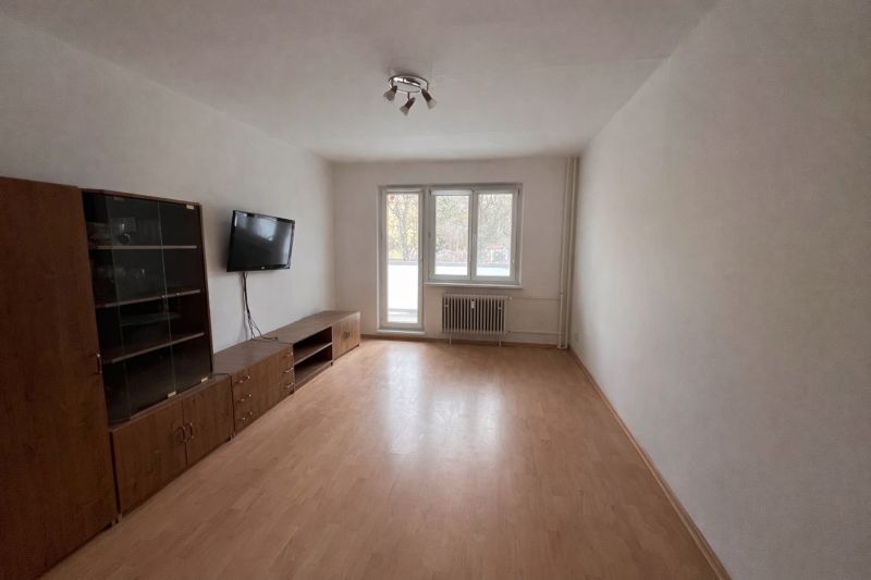 Nappali egy kétszobás lakásban, fa hatású padlóval és falra szerelt televízióval.