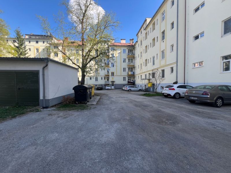 Lakóház melletti parkoló Besztercebányán autókkal és fákkal.
