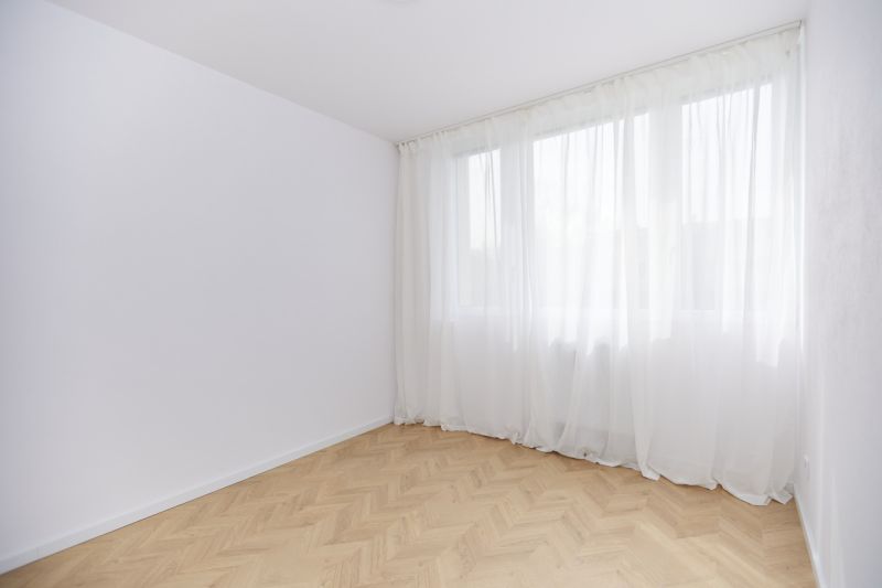 Tágas szoba fa mintázatú padlóval és fehér függönyökkel egy 4 szobás lakásban.