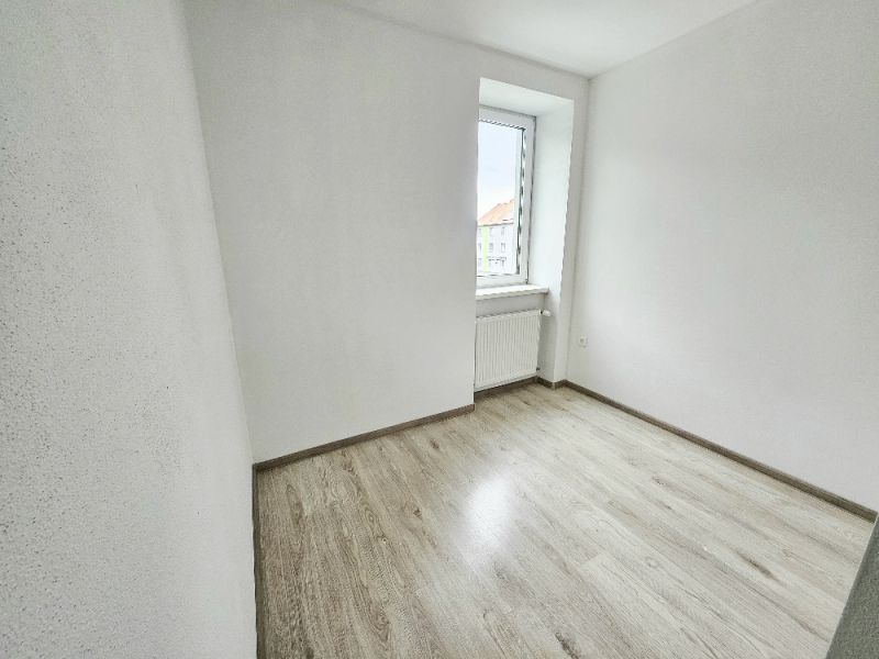 Egy szoba az egyszobás lakásban fa dekorációval ellátott padlóval és világos fallal.