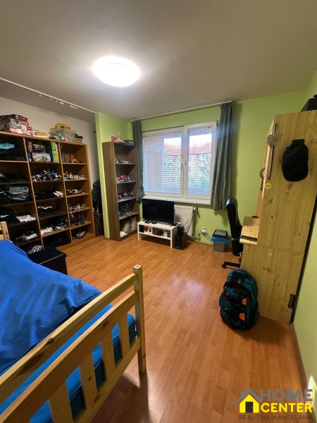 Szoba egy háromszobás lakásban polcokkal, ággyal és fa dekorációjú padlóval.