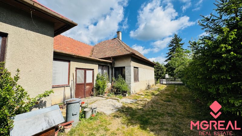 Családi ház Pažitban két bejárattal, ablakok szúnyoghálóval, mellette keskeny kert.