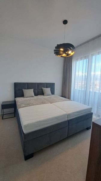 Hálószoba egy kétszobás lakásban ággyal, éjjeliszekrénnyel és függönyökkel.