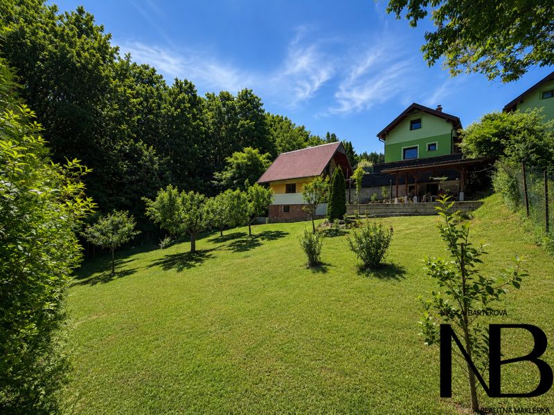 Házikó a Klučina-ban, Považská Bystrica-ban, gondozott kerttel, fákkal és zöld fűvel.