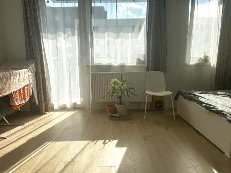 Világos szoba egy egyszobás lakásban fa dekoros padlóval és növénnyel.