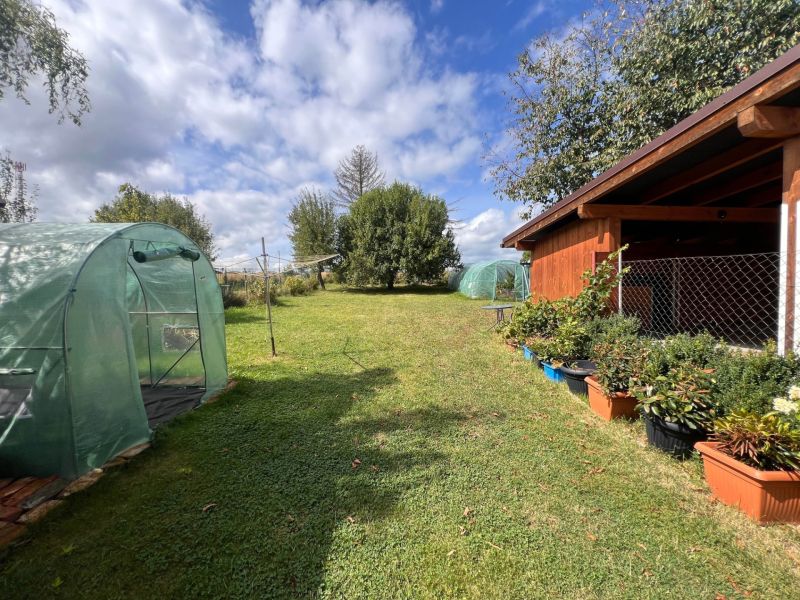 Egy családi ház kertje Bacúchon fóliasátrakkal és pavilonnal, növényekkel körülvéve.
