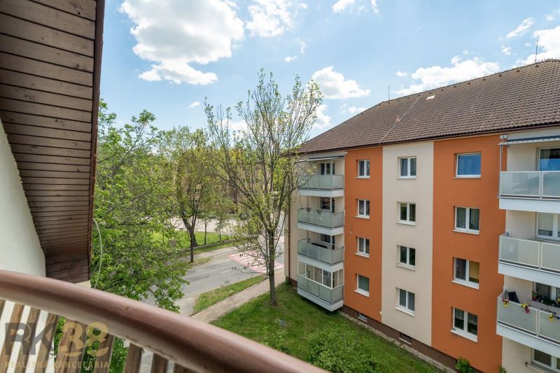 Kilátás egy háromszobás lakás erkélyéről Poprádon a környező zöldterületre és a lakóépületre.