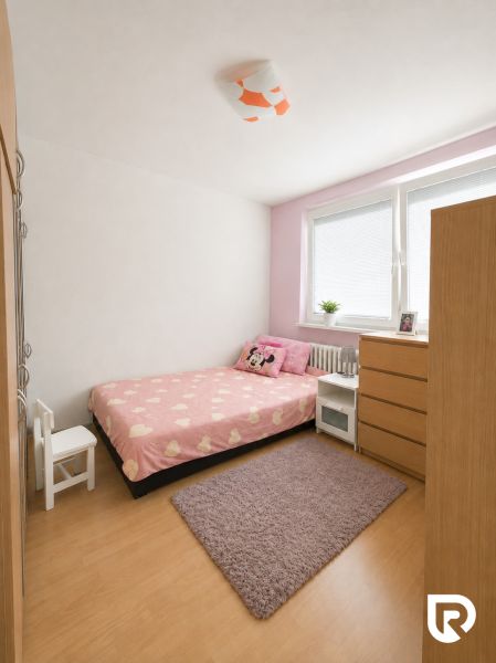 Szoba egy háromszobás lakásban rózsaszín ágyneművel, szekrénnyel és fa dekorációjú padlóval.