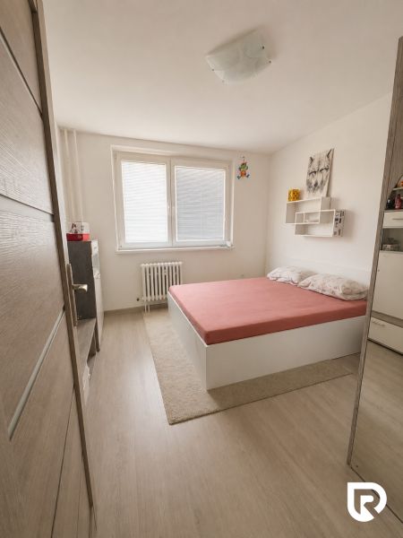 Hálószoba egy háromszobás lakásban, fa dekorációjú padlóval és egyszerű ággyal.