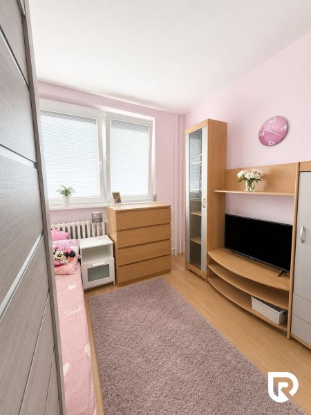 Gyerekszoba fa mintázatú padlóval, rózsaszín falakkal és fa bútorokkal egy háromszobás lakásban.