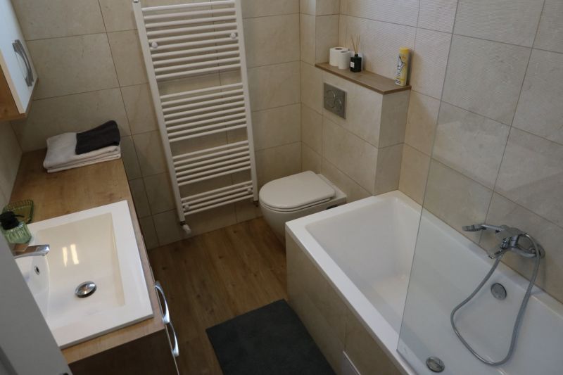 Fürdőszoba egy kétszobás lakásban káddal, mosdóval és fa dekorációjú padlóval.
