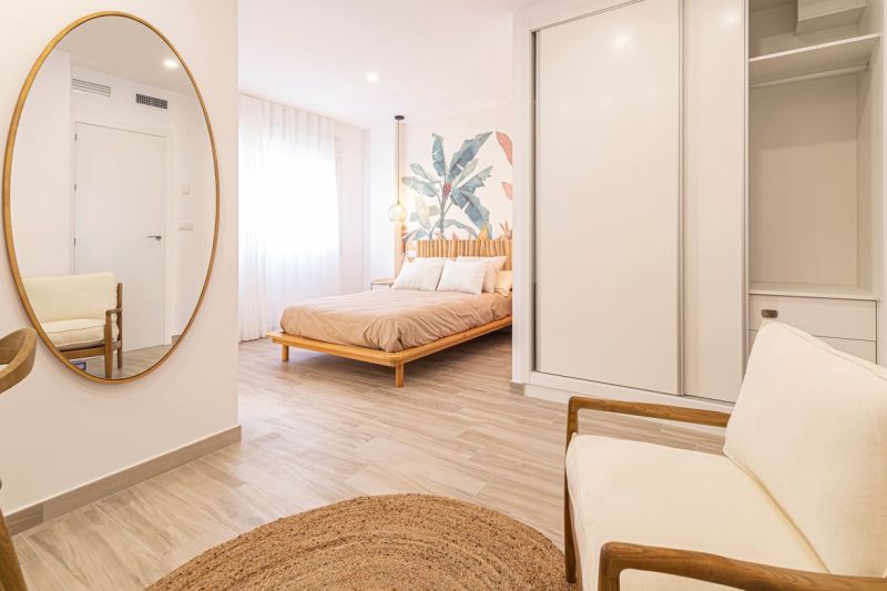 Nyaraló apartman belső tere ággyal, tükörrel és fa dekorációjú padlóval.