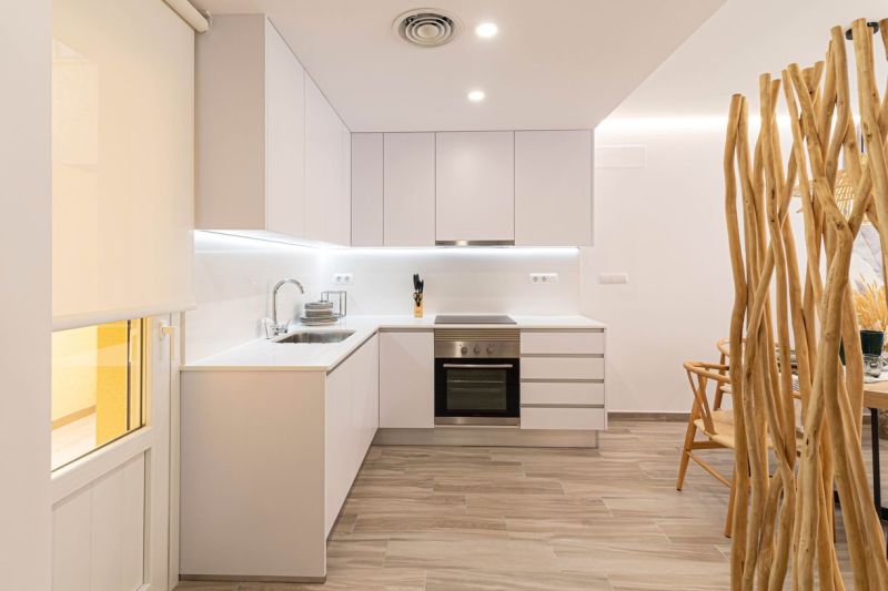 Konyha a nyaraló apartmanban fehér szekrényekkel és fa hatású padlóval.