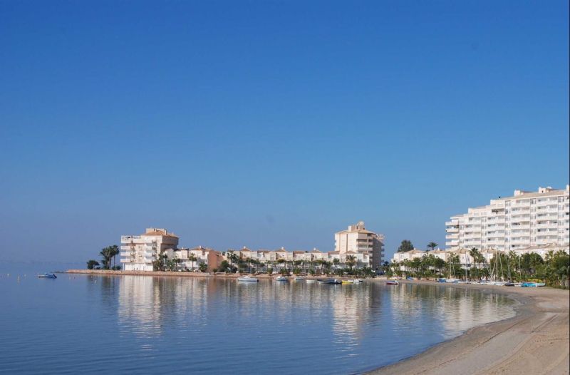 La Manga del Mar Menor tengerpartja rekreációs apartmanokkal a nyugodt tenger és a kék ég alatt.