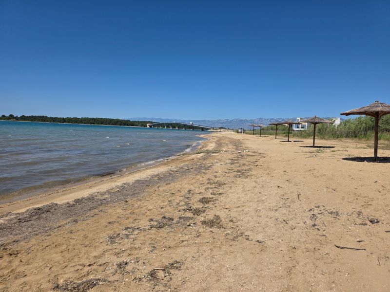 Homokos strand náderná napernyőkkel Privlakában, kék éggel és tengerrel.
