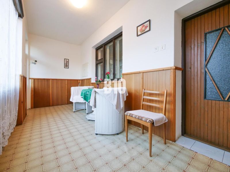 Családi ház folyosója székkel és asztallal, fa burkolatú falakkal.