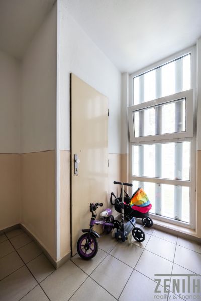 Folyosó gyerekbiciklivel az ablaknál és az ajtónál egy háromszobás lakásban.
