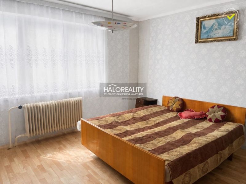 Hálószoba családi házban, fa dekorációjú padlóval és radiátorral az ablak mellett.