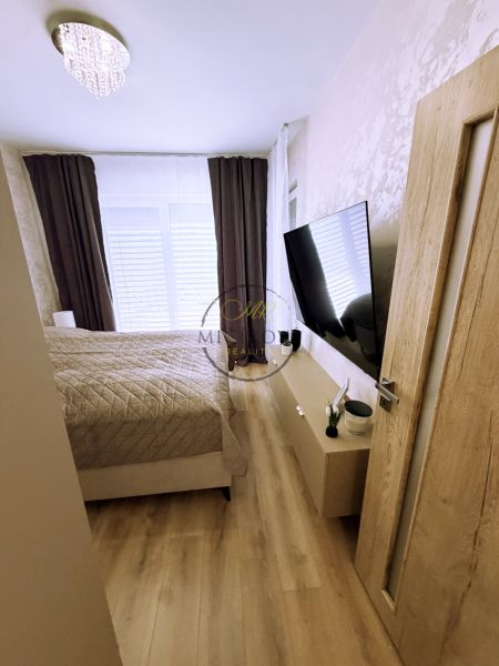 Hálószoba egy kétszobás lakásban fa dekorációjú padlóval és falra szerelt televízióval.
