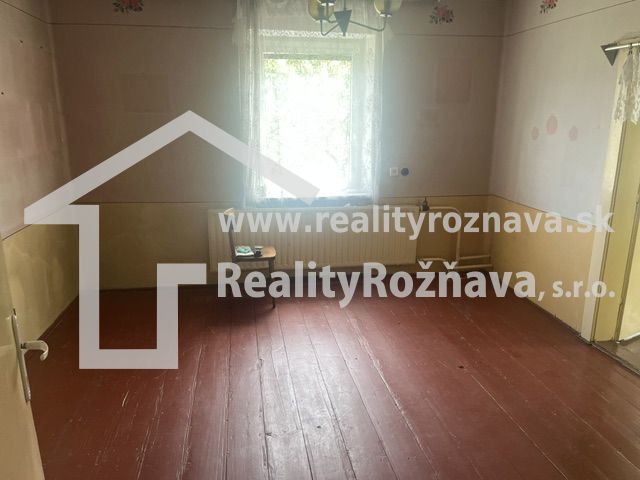 Szoba családi házban, fa padlóval, pasztell színű falakkal, fehér függönyös ablakkal.