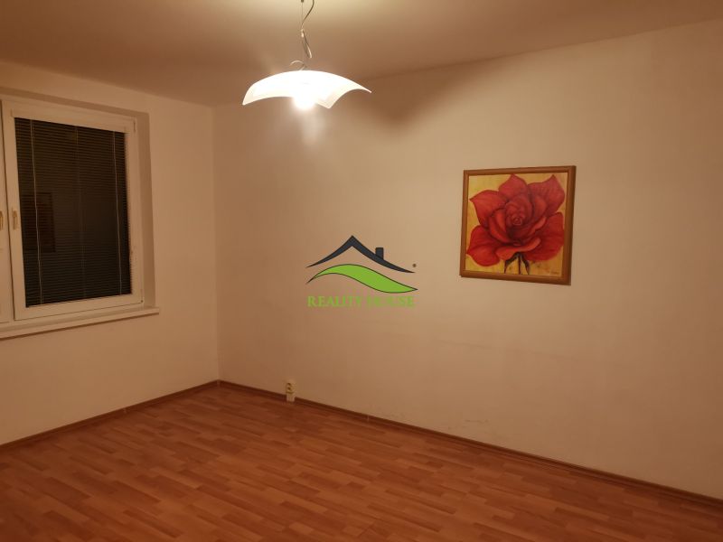 Szoba egy háromszobás lakásban, fa dekor padlóval és rózsa festménnyel.