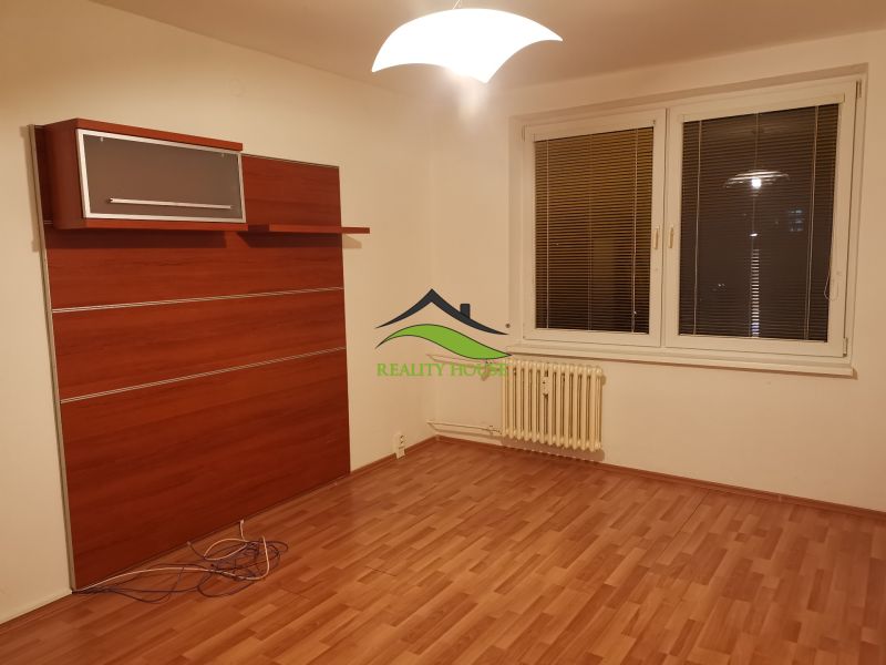 Szoba fa dekoros padlóval, fehér falakkal és fali szekrénnyel egy háromszobás lakásban.