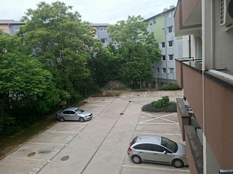 Parkoló a Dunaszerdahelyi Sport utcában autókkal és zölddel a háttérben.